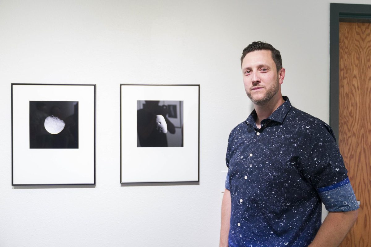 BHSU Associate Professor Skott Chandler poses with tow of his photographs on display in the Ruddell Gallery. His exhibit, "Near Misses," is inspired by the hyperreality of NASA space imagery, specifically with the Double Redirection Test Mission's images of space rocks.